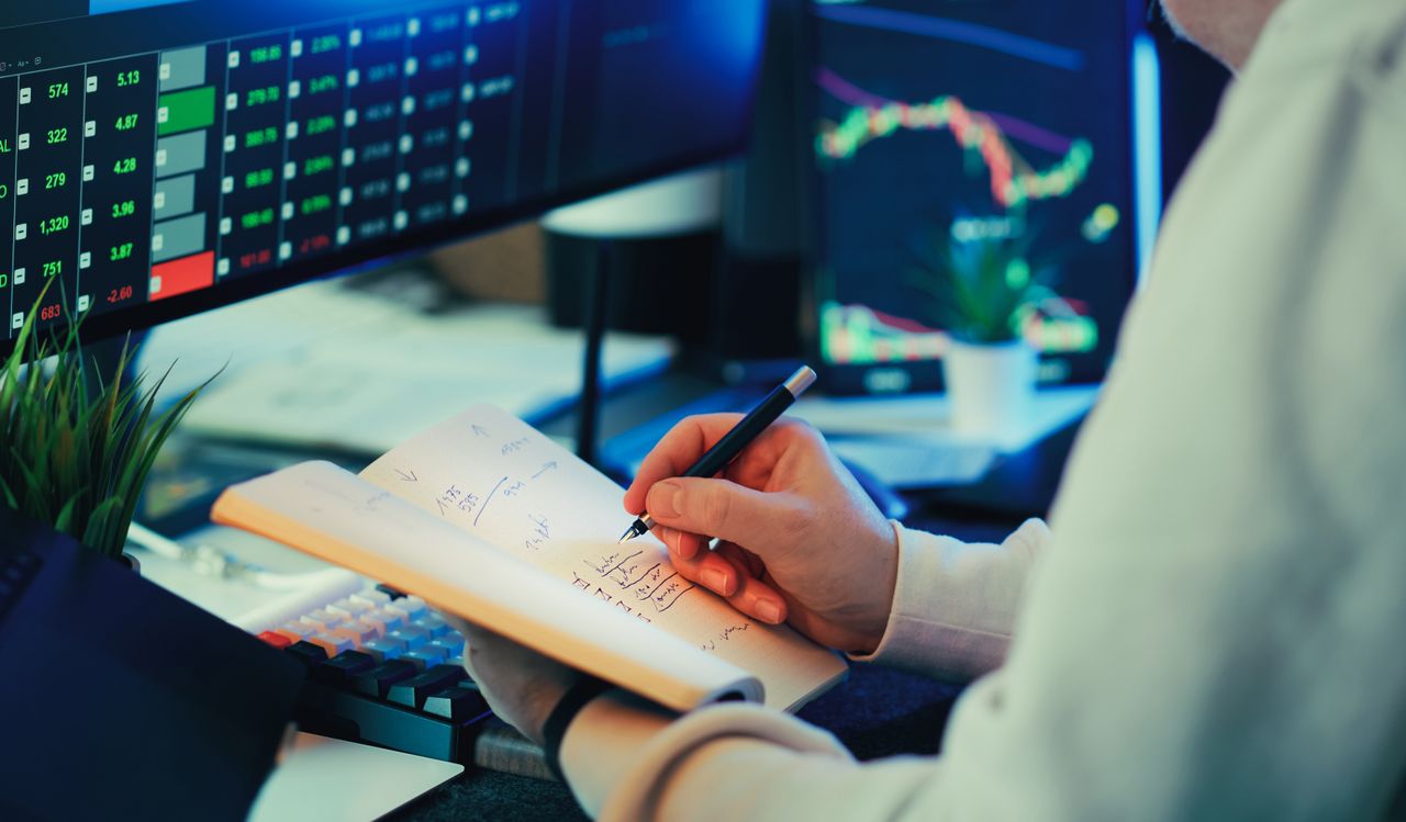 Crafting Captivating Headlines: Your awesome post title goes here Person analyzing financial data on screens, making notes. Ideal for business and finance themes.