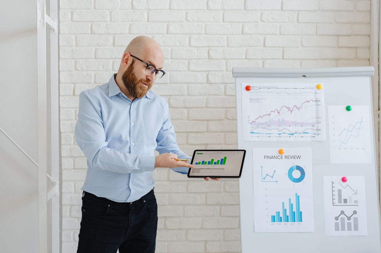 Man presenting financial data on tablet and charts indoors.